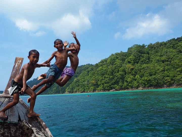 Kinder springen vor der Kulisse der Insel Koh Surin in Südthailand vom Longtailboot ins Meer der Andamanensee.
