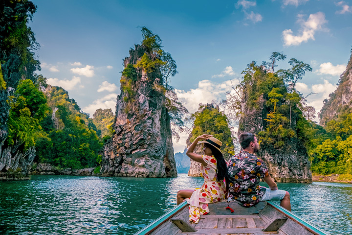 Touristen auf einer Bootstour auf dem Chiao Lan See im Khao Sok Nationalpark, bestaunen das Wahrzeichen Khao Sam Kloe.