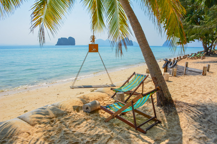 Strandstühle beim Coco Cottage Resort auf Koh Hai unter Palmen.